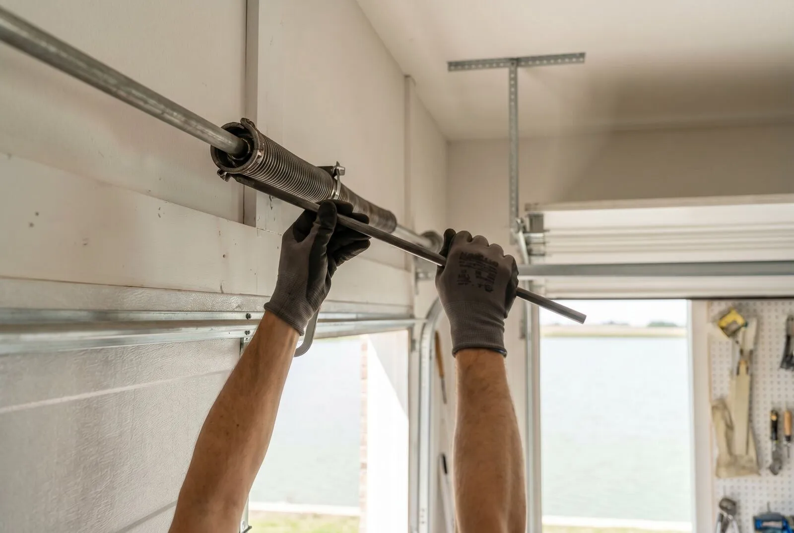 A technician's gloved hands working with winding bars at a torsion spring